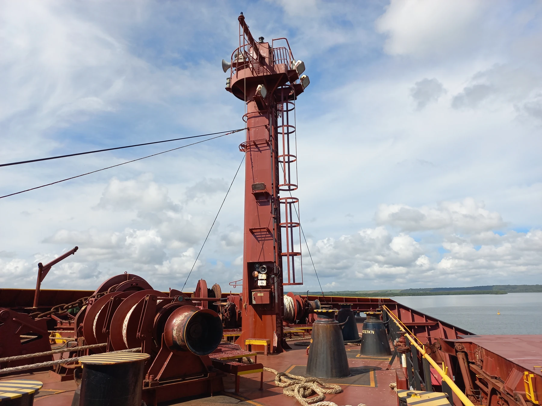 A ship's deck with a mast, mooring equipment, and the Cabedelo port river in the background.